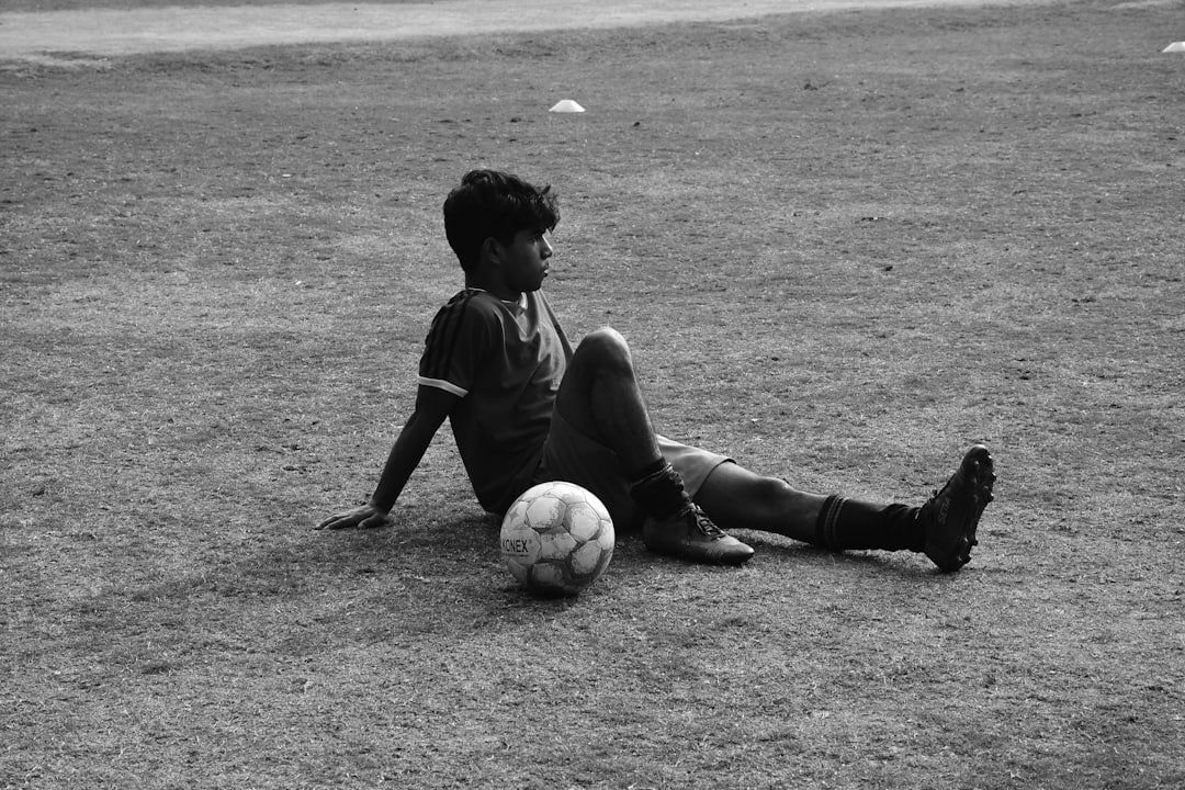 un-jeune-garcon-assis-sur-le-sol-avec-un-ballon-de-football-eSoxqiL_vCA